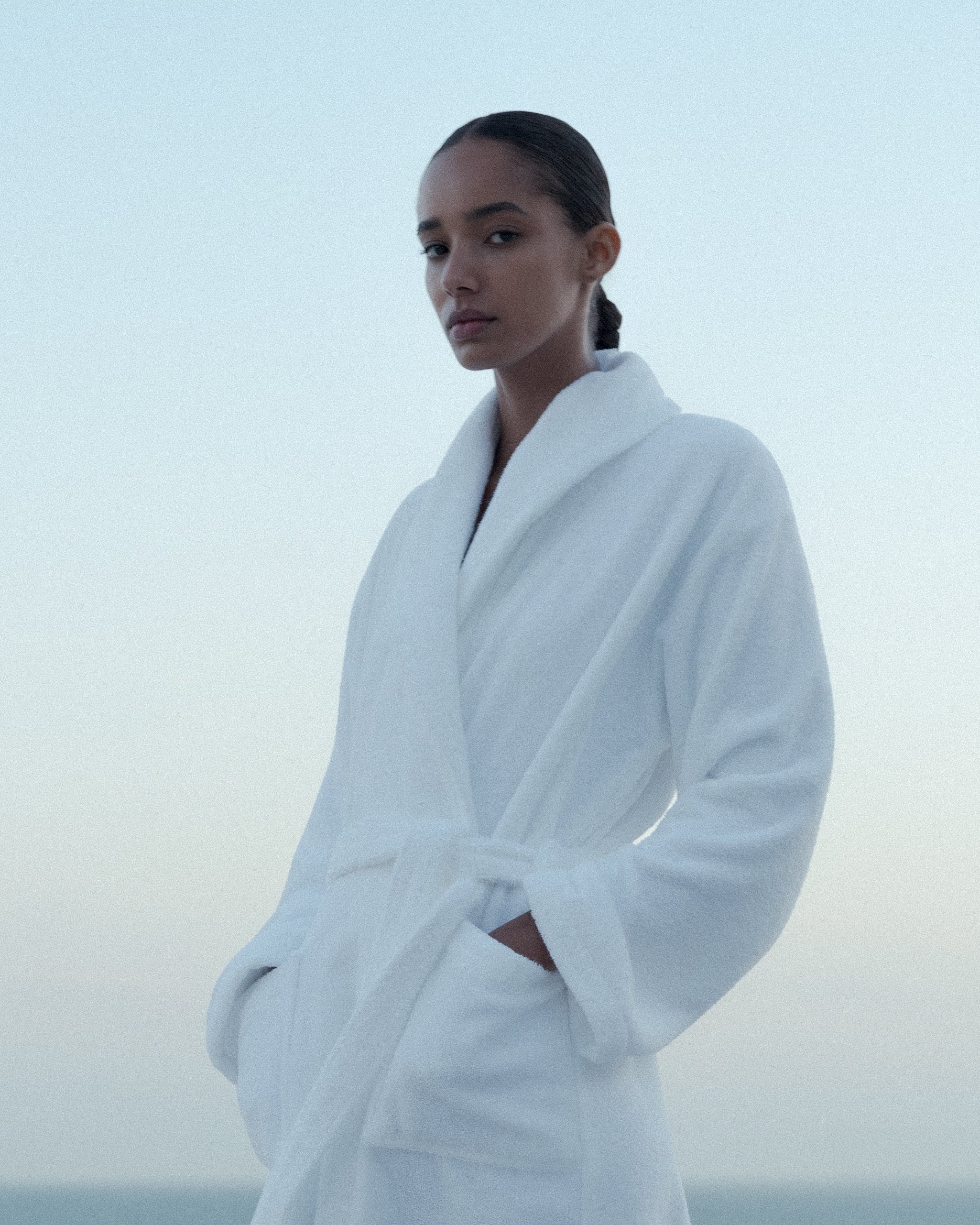 Closeup of a woman dressed in a soft terry white bath rope with a soft and light blue skye background.