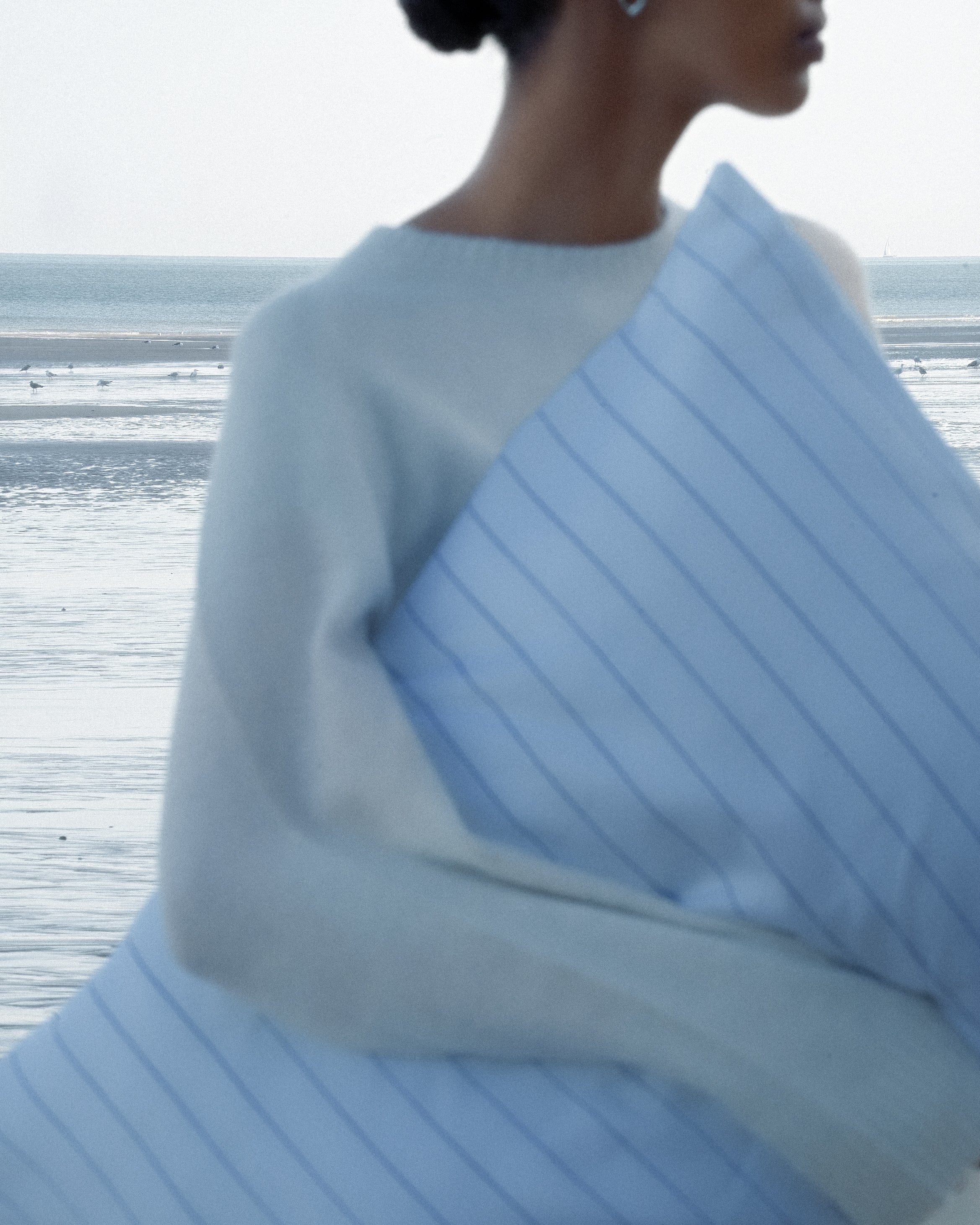Blurry image of woman holding a pinstripe pillow and ocean background