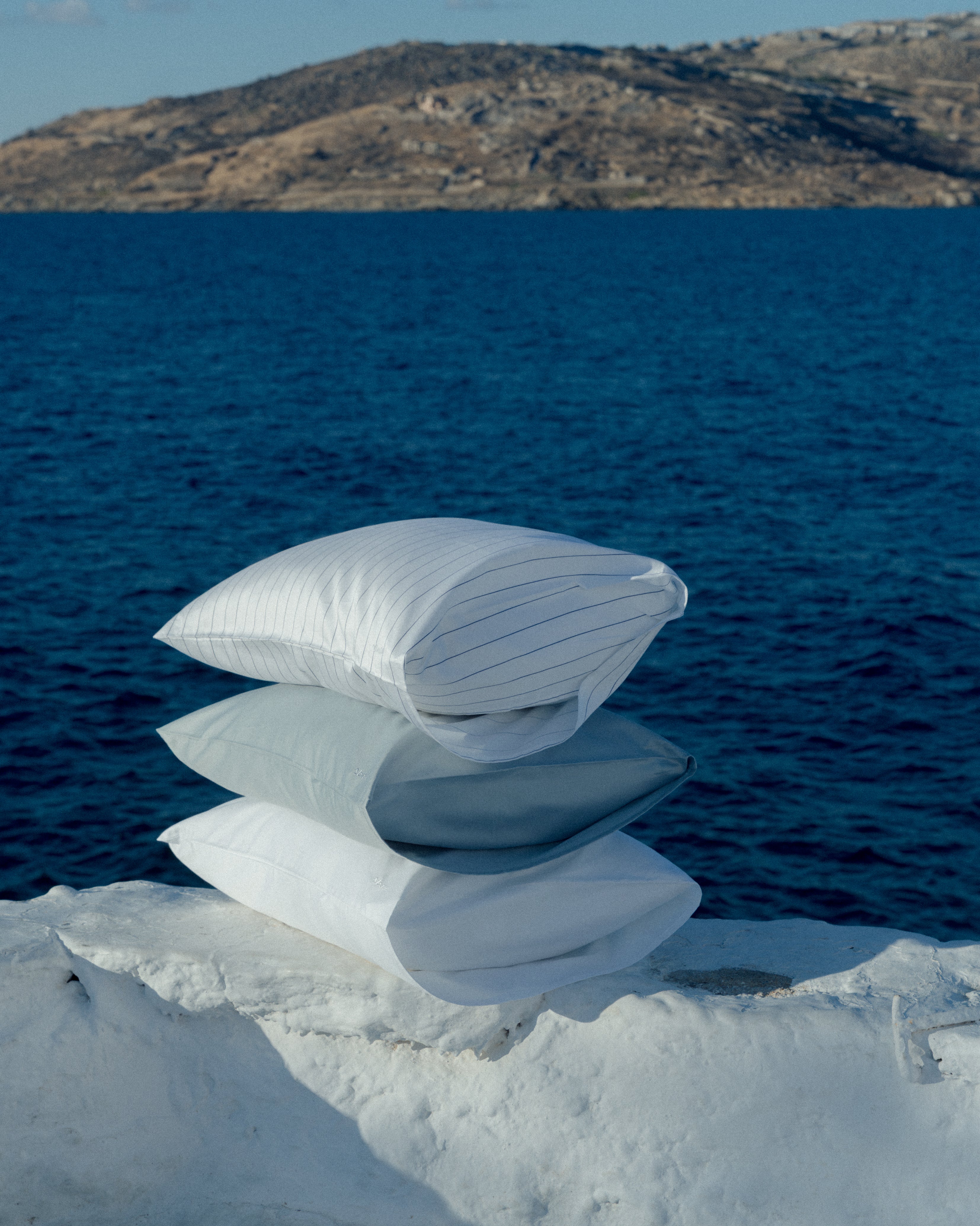 3 pillows standing next to each other in light colors with the blue ocean behind them.