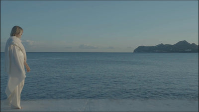 Woman walking on the beach with the blue ocean behind her. 